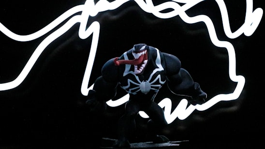 A black and white action figure stands against a backdrop of white, wavy neon-like lines on a dark background. The figure has a large, open mouth with red details and is designed with a muscular build.