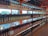 Shelves filled with various bottles of wine arranged in rows, displaying different labels and colors. The setting is an indoor store with large windows allowing natural light to illuminate the bottles from behind.