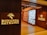 A well-lit retail store entrance features the sign 'Bonanza Satrangi' on a wooden wall. Inside, the store has neatly arranged shelves filled with bottles and boxes, suggesting a display of perfumes or beauty products. The interior is warmly illuminated, enhancing the inviting atmosphere.