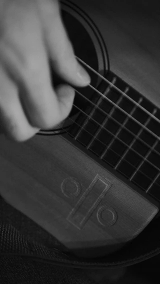 Black and white close-up photo of muao playing guitar on stage, spotlight highlighting fingers on strings.