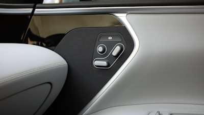 Detail image of a car door interior, featuring an array of seat adjustment controls. The panel includes multiple buttons and switches against a dark background, with the overall design showcasing a blend of sleek, modern aesthetics.