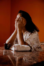 a woman sitting at a table covering her face with her hands