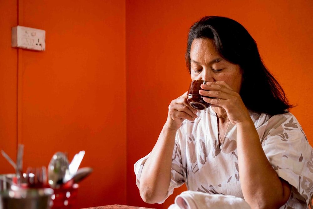 a woman sitting at a table drinking a cup of coffee