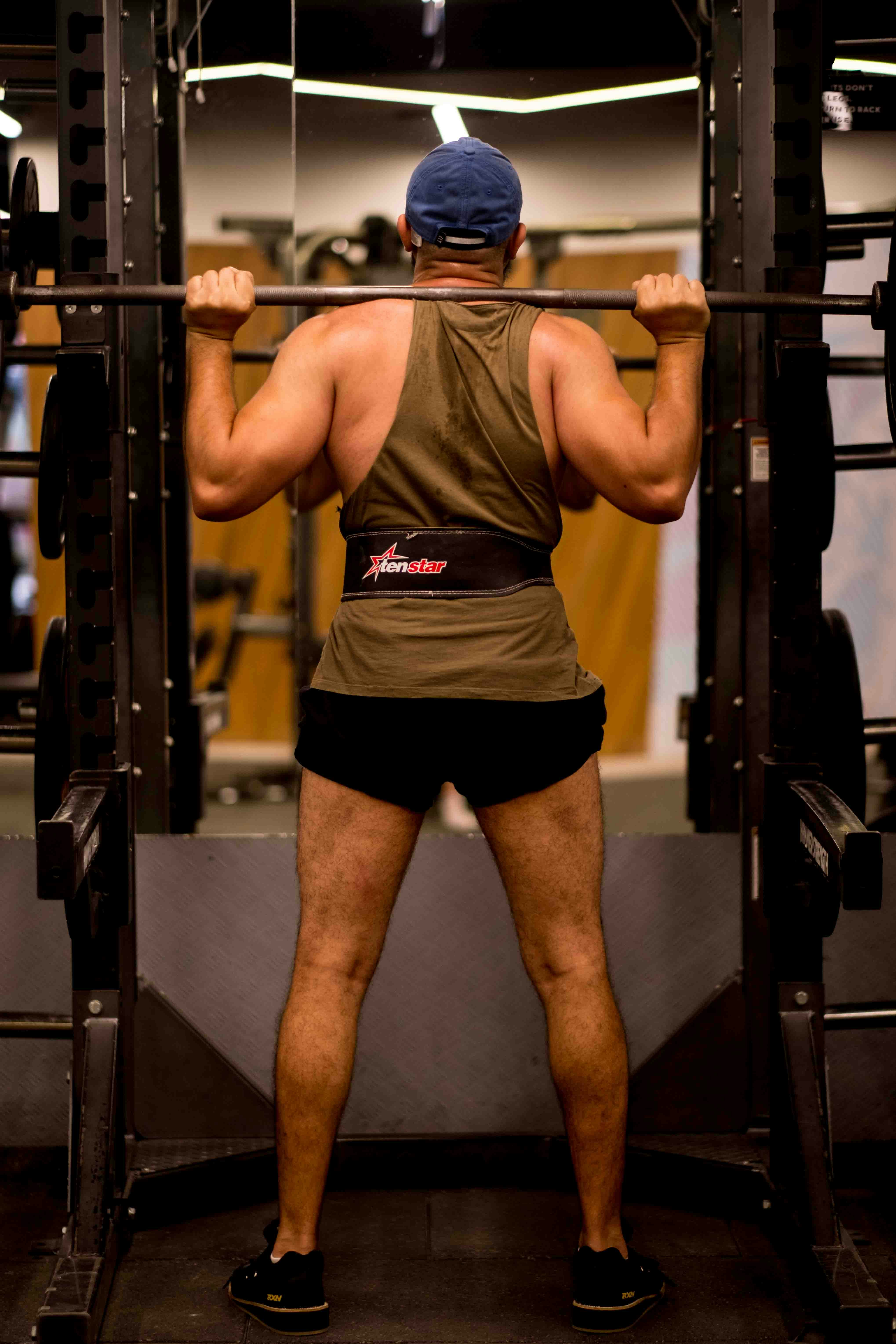 a man in shorts and a baseball cap lifts a barbell