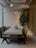A modern dining area features a long stone table surrounded by stylish wooden chairs with woven seats. Industrial lighting hangs from the ceiling, adding an elegant touch. A tall green plant in the corner adds a natural element to the space. The walls are a combination of wood paneling and light-colored textured surfaces, contributing to a contemporary and clean ambiance.