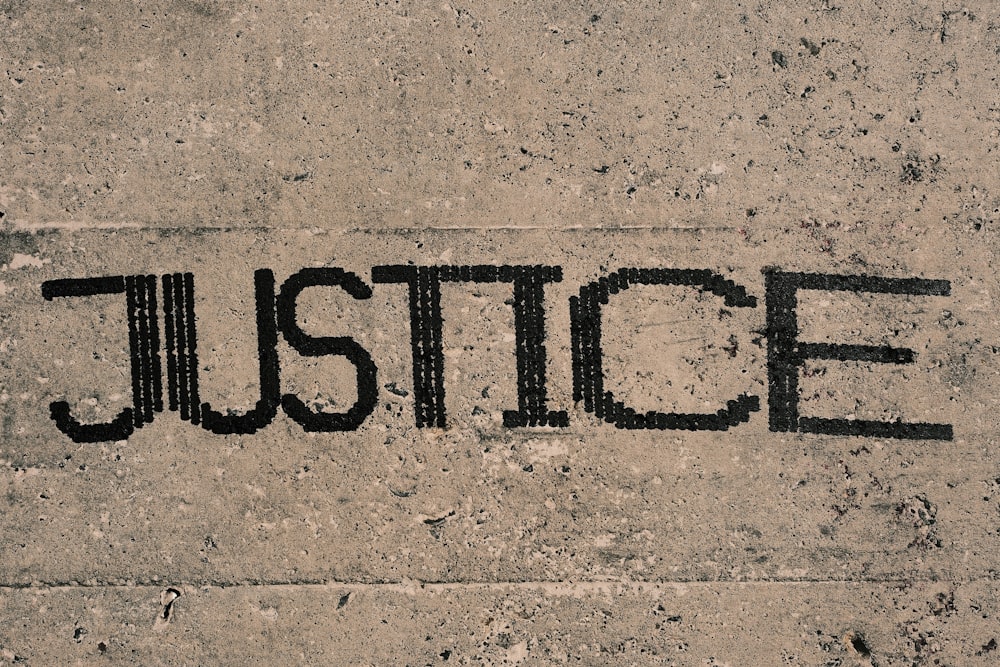 the word justice written in black ink on a concrete surface