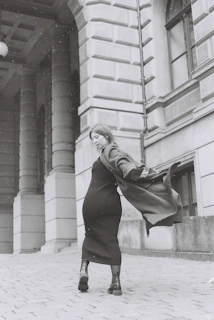 Woman strolling through a cobblestone street wearing a rich burgundy coat with intricate embroidery