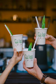 A joyful moment of a customer holding a custom-printed plastic cup outdoors with greenery background.