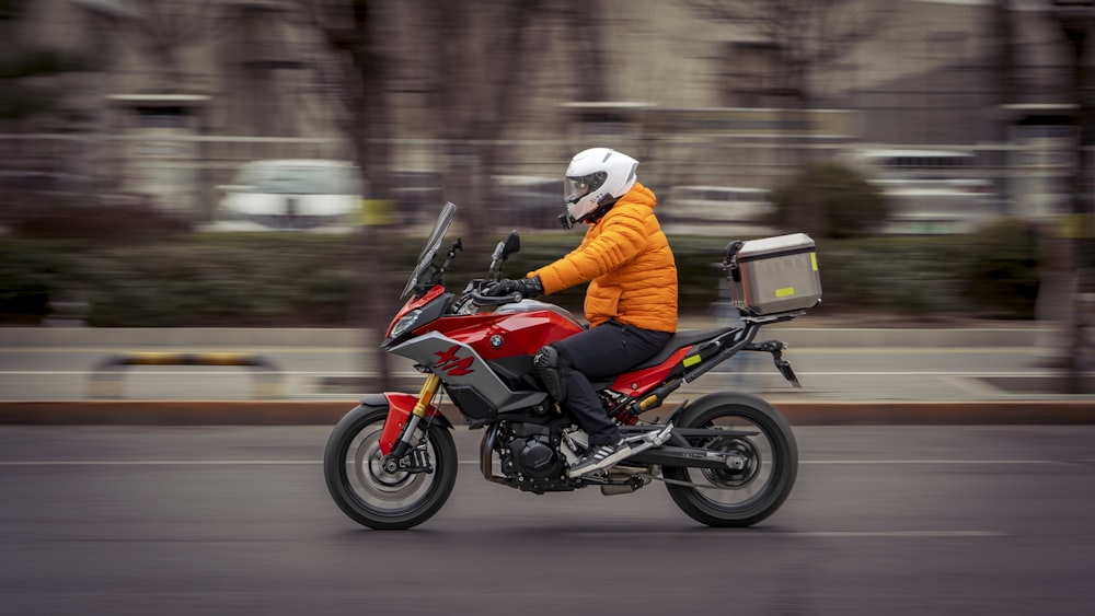 a man riding a red motorcycle down a street