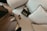 An elegant setting featuring a black handbag with gold chain detailing and bold lettering next to a pair of stylish sunglasses. The items are placed on a plush white cushion with black piping that rests on a light-colored wooden floor.