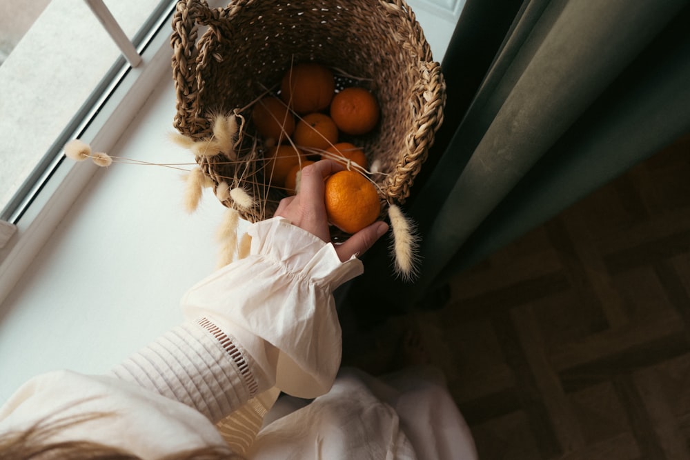 a person holding a basket of oranges in front of a window