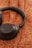 A pair of black over-ear headphones lies on a textured brown surface. The headphones have a sleek design with cushioned ear cups and a visible brand logo printed in gold.