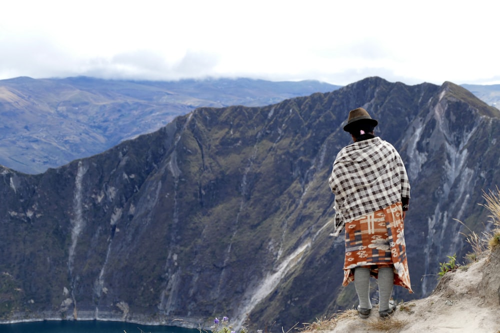 a man standing on top of a mountain next to a lake