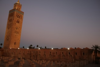 Two tall, elegant towers against a twilight sky, with gold-lit windows and traditional Emirati patterns subtly incorporated into the facade.