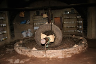 Rustic grinding mill surrounded by sacks of natural grains and spices in a sunlit room.