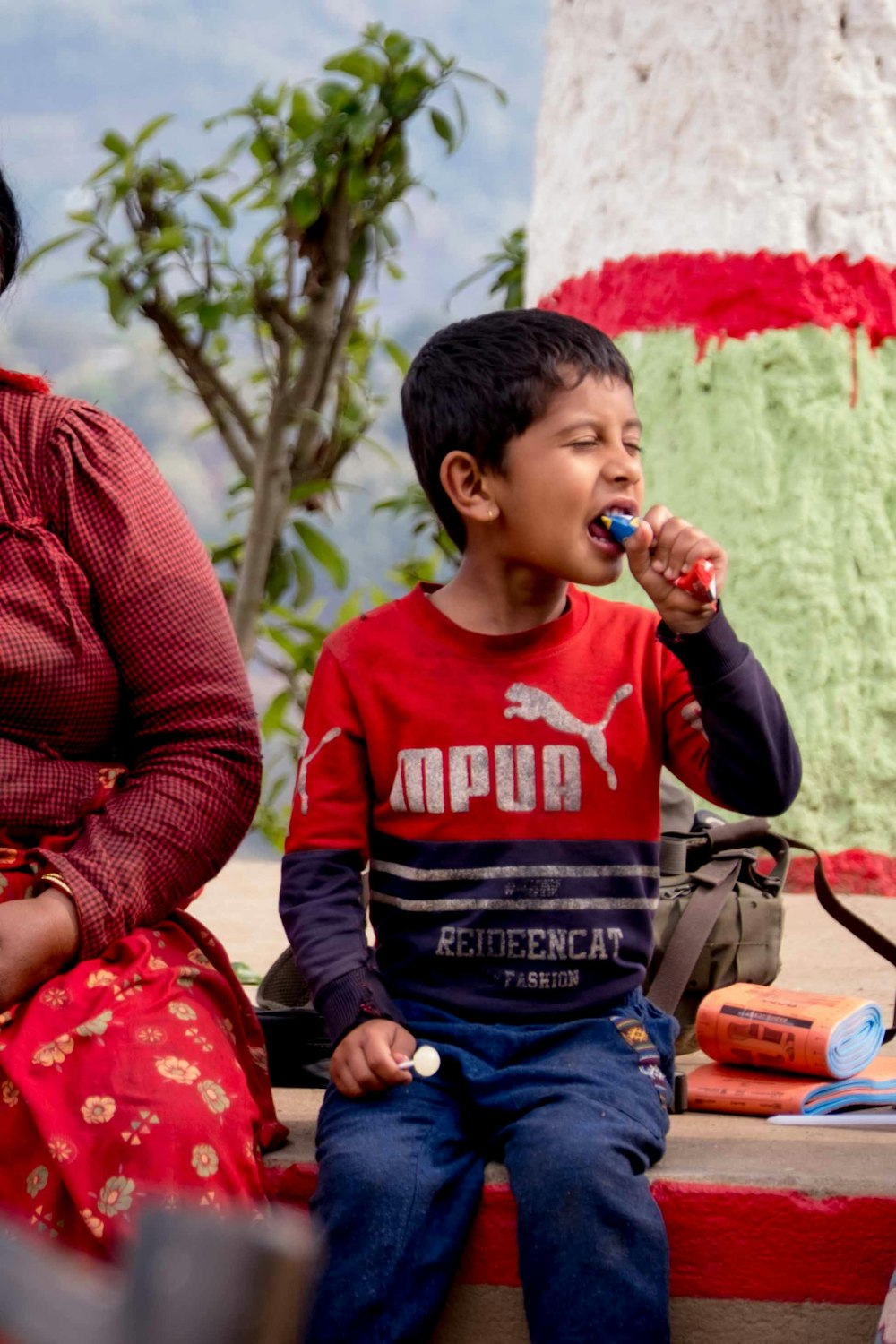 a woman sitting next to a boy who is brushing his teeth