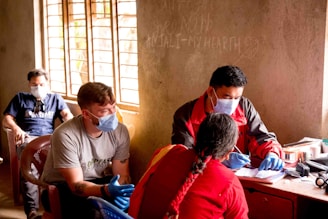 a group of people sitting around a table wearing masks