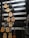 A wall displaying various acoustic guitars arranged in rows. The guitars differ in color and design, including shades of natural wood, black, and sunburst. Each guitar hangs on hooks attached to horizontal strips. The background is dark with white strips horizontally aligned, enhancing the visibility of the guitars.
