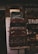 A stack of vintage suitcases is displayed against a brick wall. The top suitcase is labeled with 'Air France'. Behind the suitcases, a shop window showcases various antiques, including jars, figurines, and a violin.