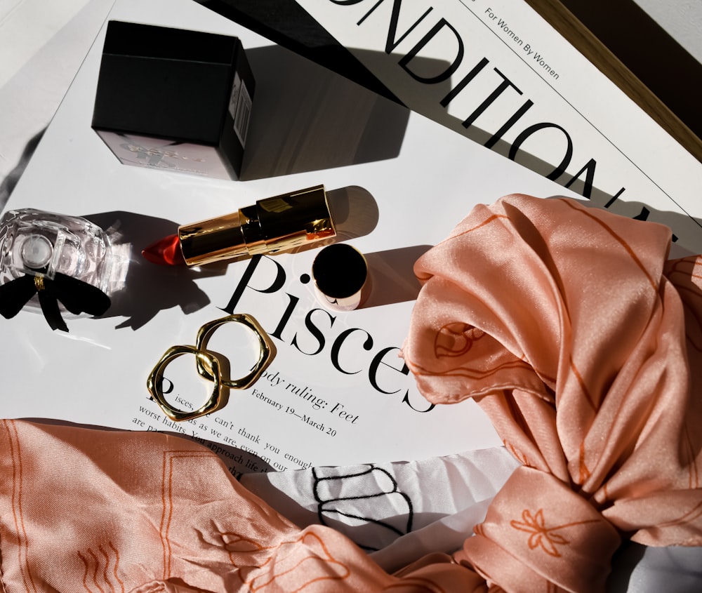 a table topped with a ring, lipstick, and a magazine
