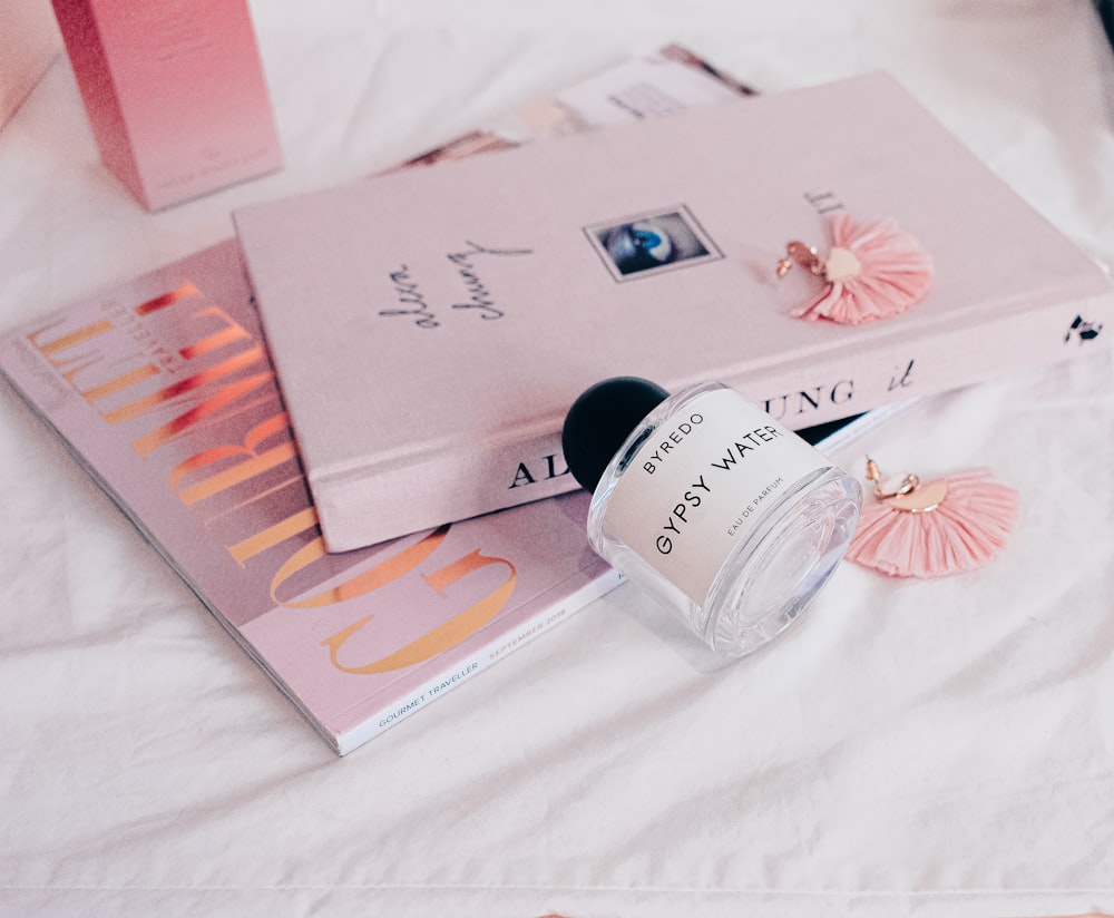 Una botella de perfume sentada encima de una cama junto a un libro