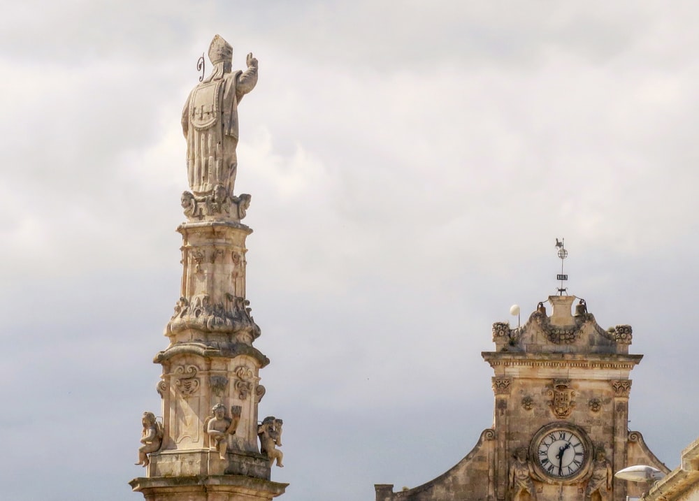Una estatua alta se encuentra junto a una torre del reloj