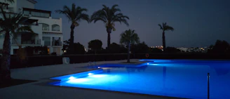 A serene backyard pool lit by underwater blue lights during twilight.