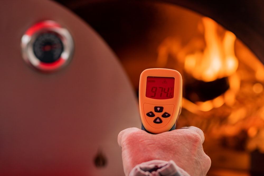 eine Person, die ein Thermometer vor einem Feuer hält