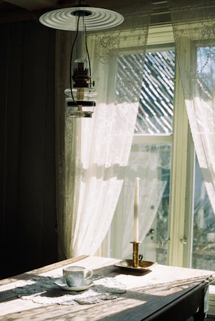 A gentle morning light filtering through lace curtains onto a wooden table with a Bible and fresh flowers.
