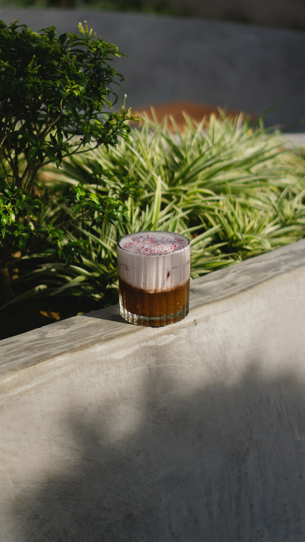 a glass of beer sitting on a ledge next to a bush