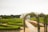 A beautifully landscaped garden with geometric hedges and pathways leading towards a large, domed greenhouse structure. People are walking along the paths, enjoying the serene environment. The garden is lush with greenery and vibrant flower beds. The sky above is overcast, providing a soft light over the scene.
