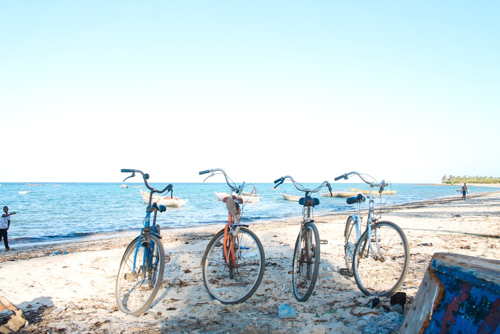 three bicycles parked on a beach next to the ocean