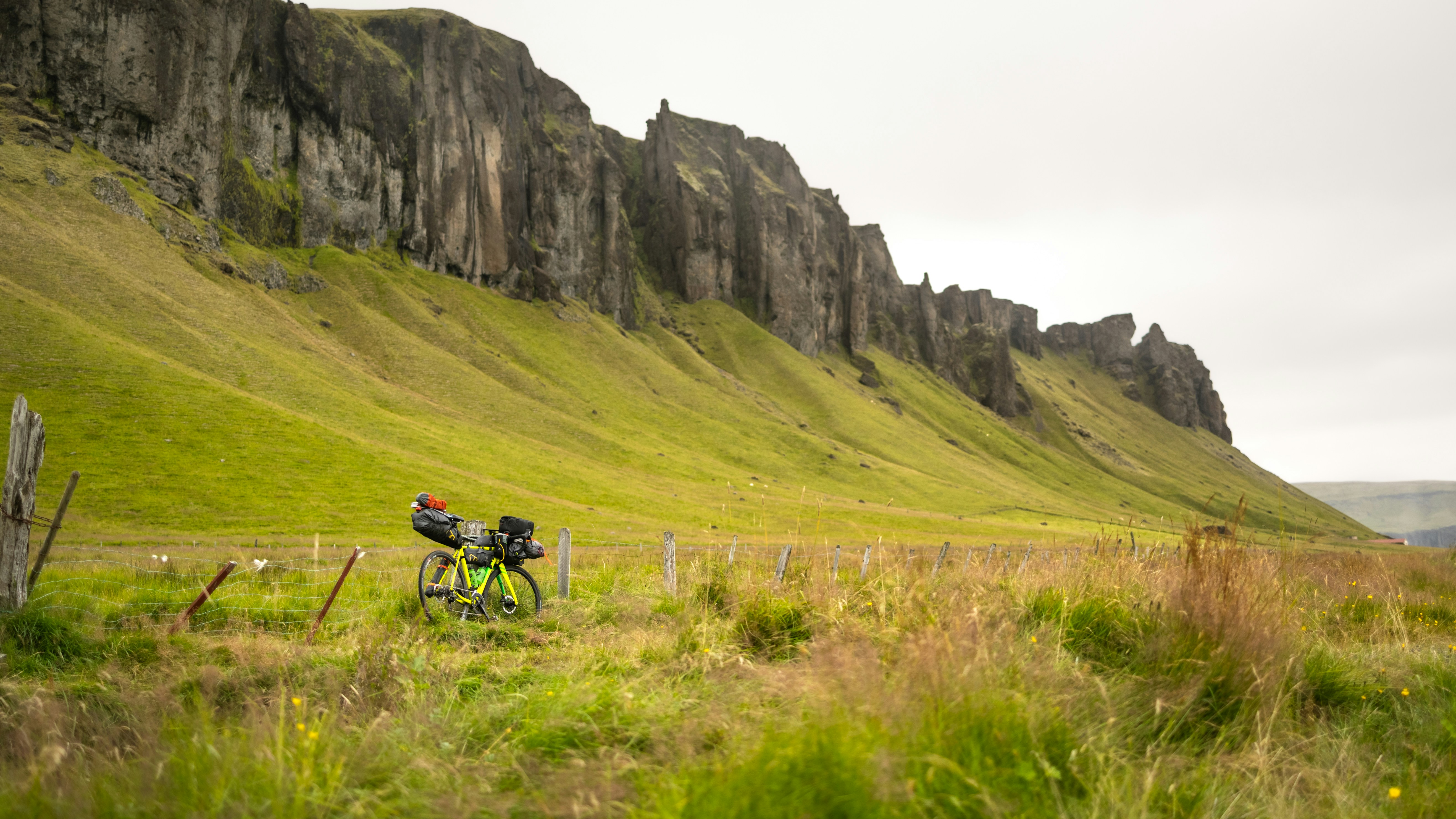 Fully loaded bikepacking bike leaning against a wooden fence on a gravel trail surrounded by mountains
