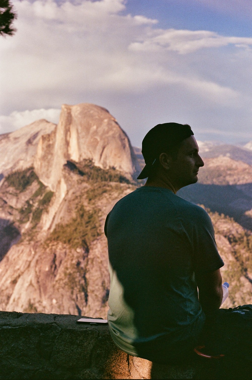 a man sitting on a ledge looking at a mountain