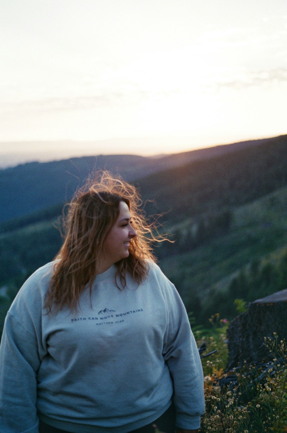 a woman standing on top of a lush green hillside