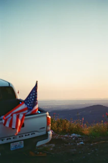 A patriotic t-shirt draped over a vintage pickup truck’s tailgate with an open highway in the background.