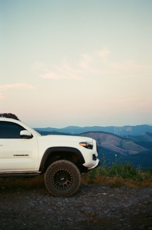 A 4WD jeep parked on a rugged volcanic trail with the first light of dawn breaking over Mount Batur.