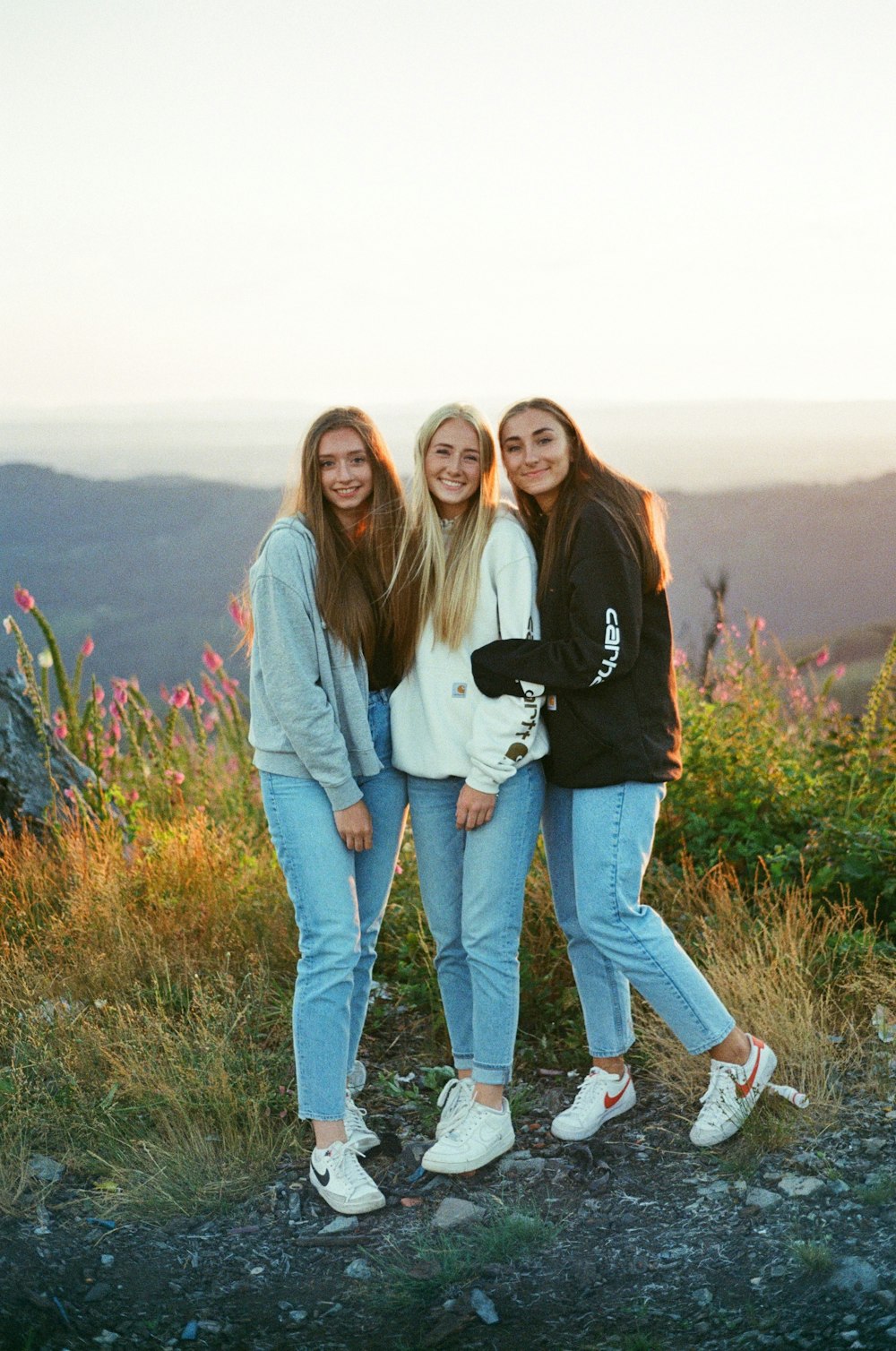 três meninas estão posando para uma foto no topo de uma montanha