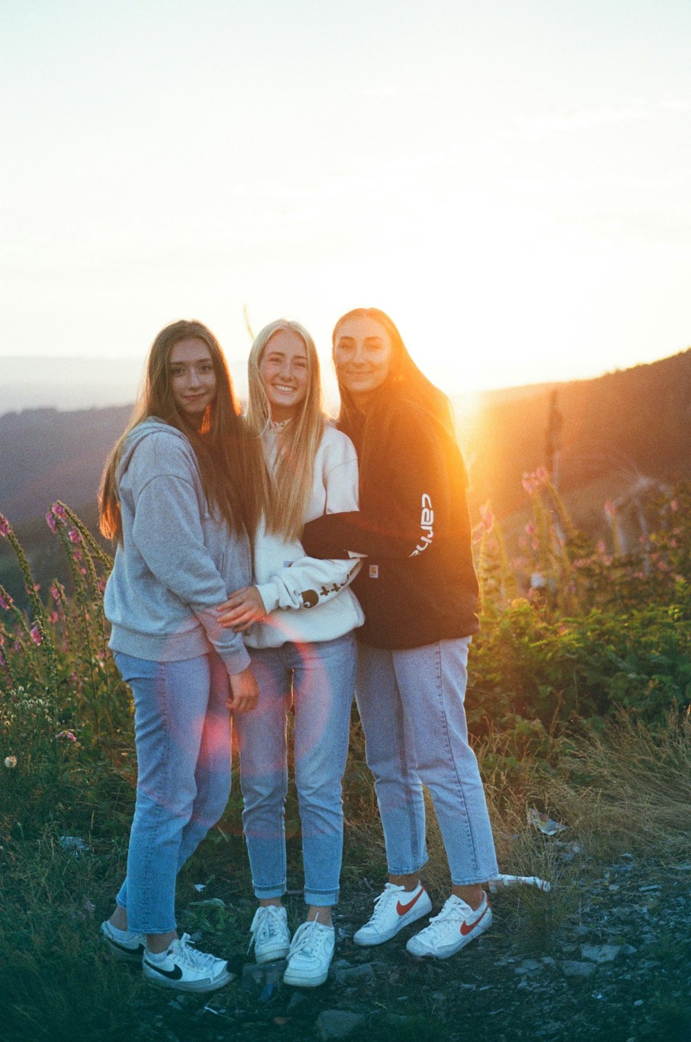 three girls are standing on a hill at sunset