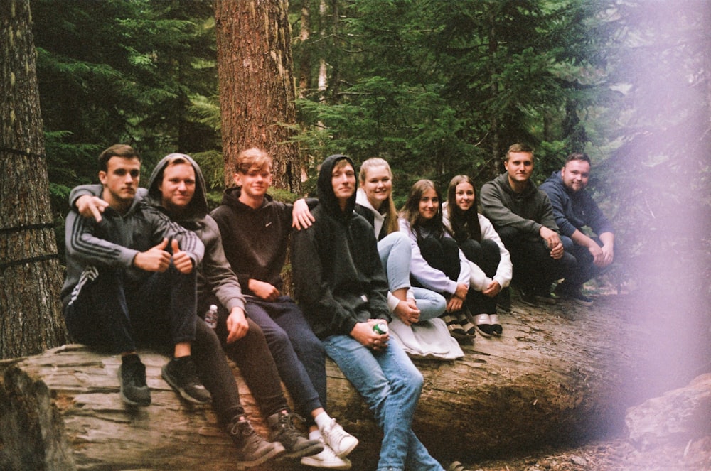 a group of people sitting on a log in the woods