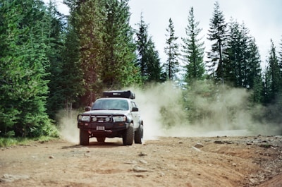 An off-road ATV kicking up dust on a rugged trail surrounded by pine trees under a bright blue sky.