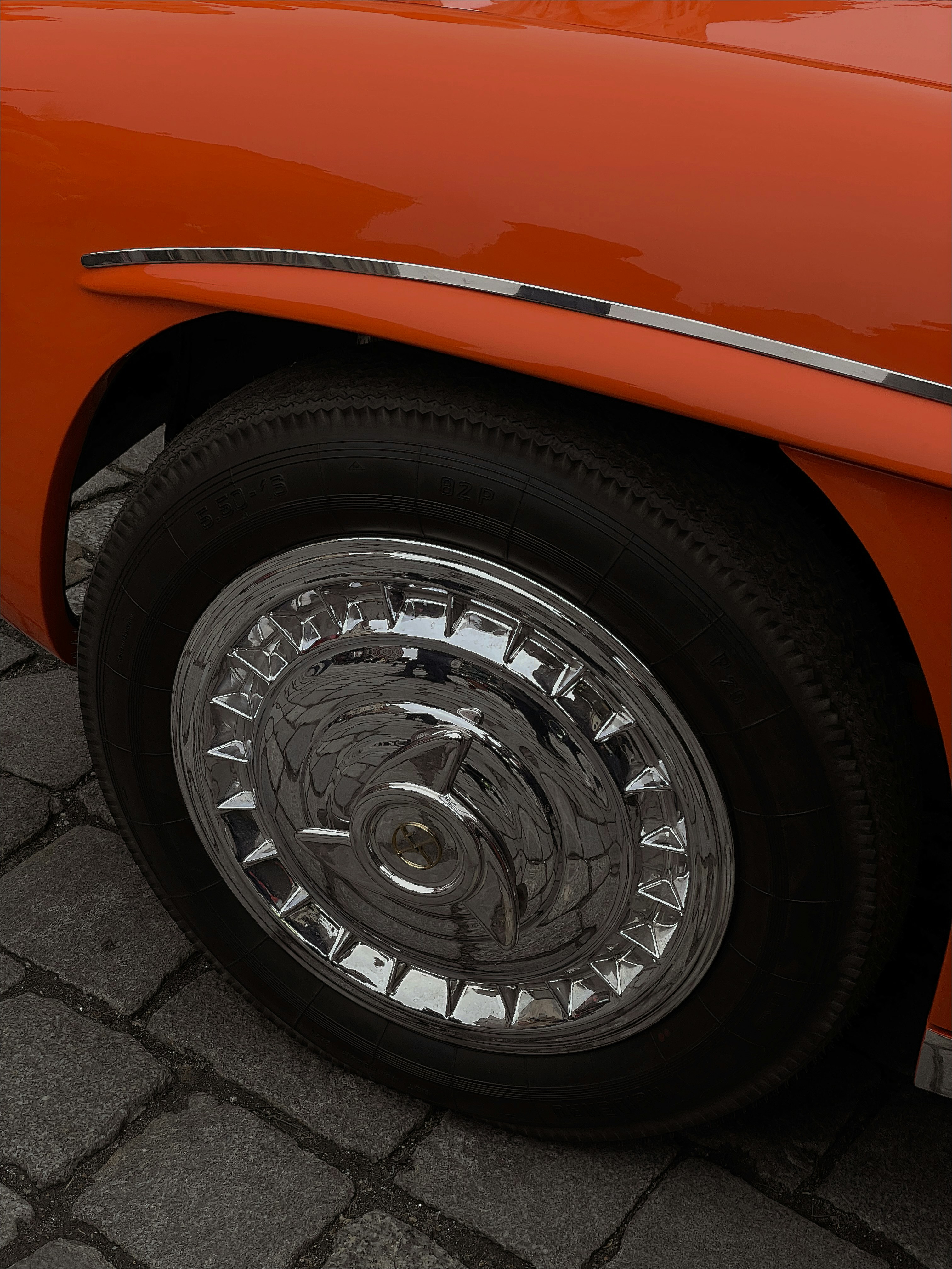 Set of shiny chrome hubcaps reflecting sunlight on a vintage Beetle wheel.