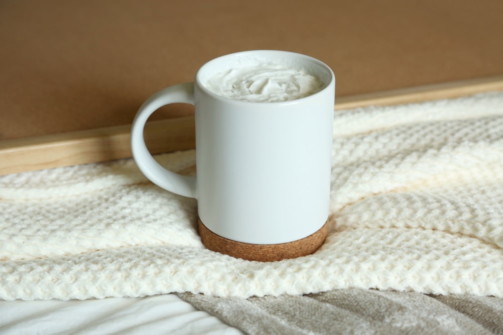 a white coffee cup sitting on top of a bed