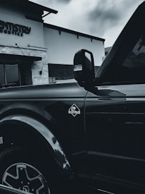 A black vehicle is parked in front of a building with signage that reads 'Dentistry.' The vehicle's side view mirror and part of the door are visible, along with the 'Outer Banks' emblem. The architecture of the building includes stone and brick elements.