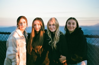 A diverse group of four happy people smiling together against a radiant sunrise background.