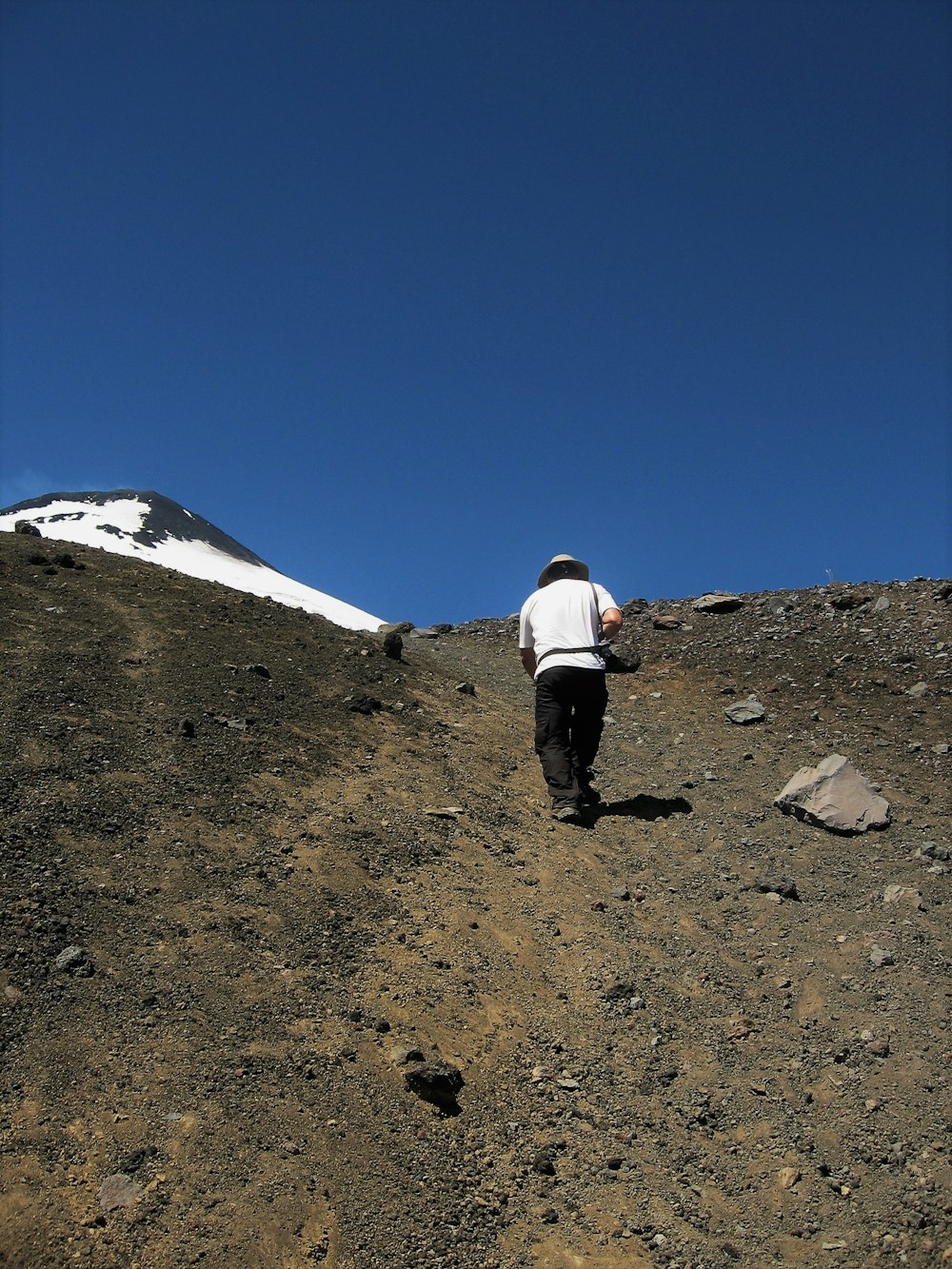 a person walking up a hill with a snow covered mountain in the background