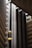 An interior view of a modern building featuring a sleek, vertical elevator shaft with glass elevators and balconies. The architecture showcases geometric patterns with a mix of concrete and metal elements. Soft lighting adds a warm ambiance to the scene.