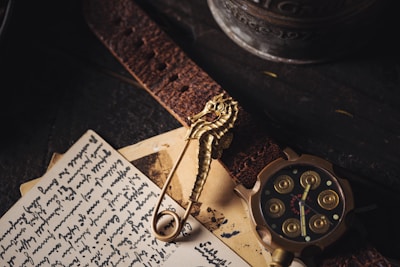 An assortment of vintage items including a seahorse-shaped brooch, a leather strap, a handwritten letter, and a round, intricately designed watch with golden accents. The scene is dimly lit against a dark wooden surface, adding a sense of nostalgia.