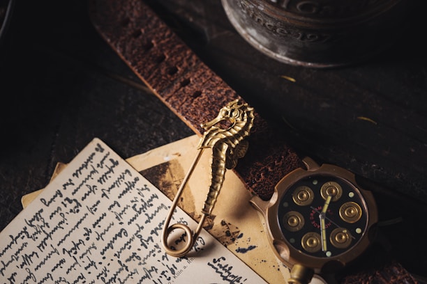 An assortment of vintage items including a seahorse-shaped brooch, a leather strap, a handwritten letter, and a round, intricately designed watch with golden accents. The scene is dimly lit against a dark wooden surface, adding a sense of nostalgia.