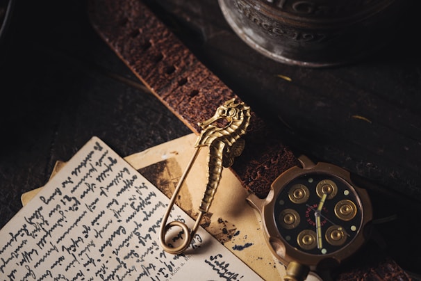 An assortment of vintage items including a seahorse-shaped brooch, a leather strap, a handwritten letter, and a round, intricately designed watch with golden accents. The scene is dimly lit against a dark wooden surface, adding a sense of nostalgia.